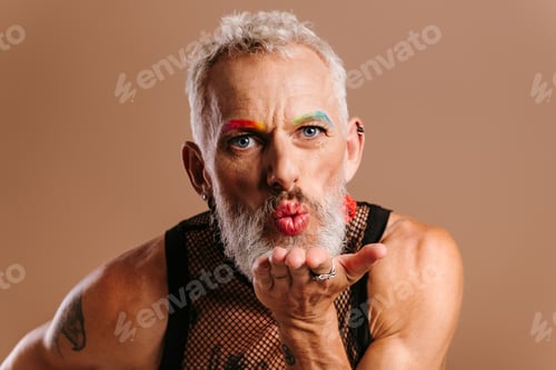 Preview: Portrait of bearded mature gay man with make-up blowing a kiss against brown background