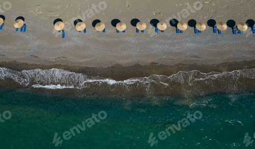 Preview: Aerial view from a flying drone of beach umbrellas in a row on an empty beach with braking waves