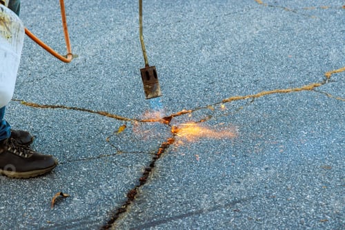 Preview: Road surface restoration work in the worker performs on burning dry grass in asphalt cracks before