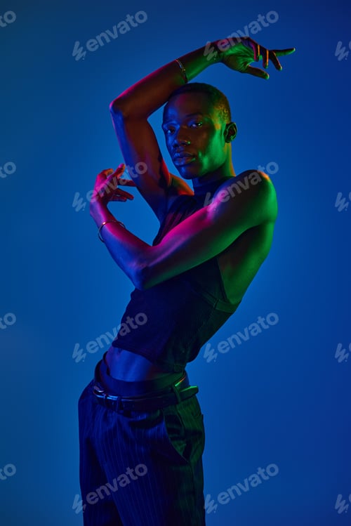 Preview: Stylish young man poses dramatically under vibrant blue and green lighting in a studio setting