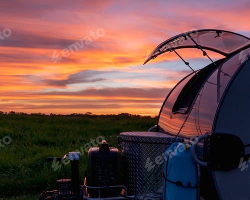 Preview: Beautiful shot of a bright colorful sunset on a field with camping equipment