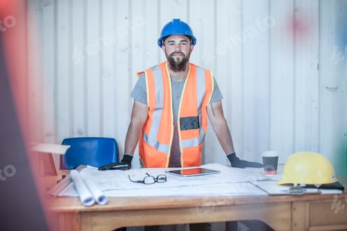 Preview: Portrait of young male construction worker standing at desk in portable cabin