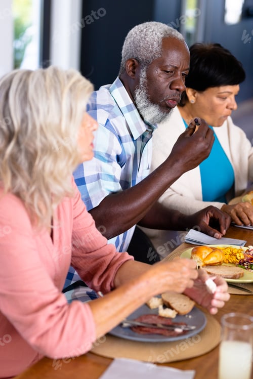 Preview: African american senior man eating lunch with multiracial female friends at dining table