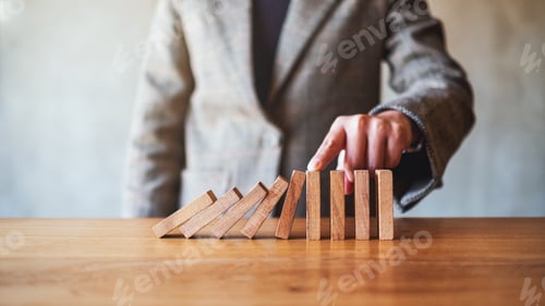 Preview: a businesswoman's finger try to stopping falling wooden dominoes blocks