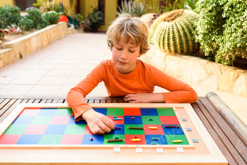 Preview: Student boy using a montessori checker board outdoors doing homeschooling.