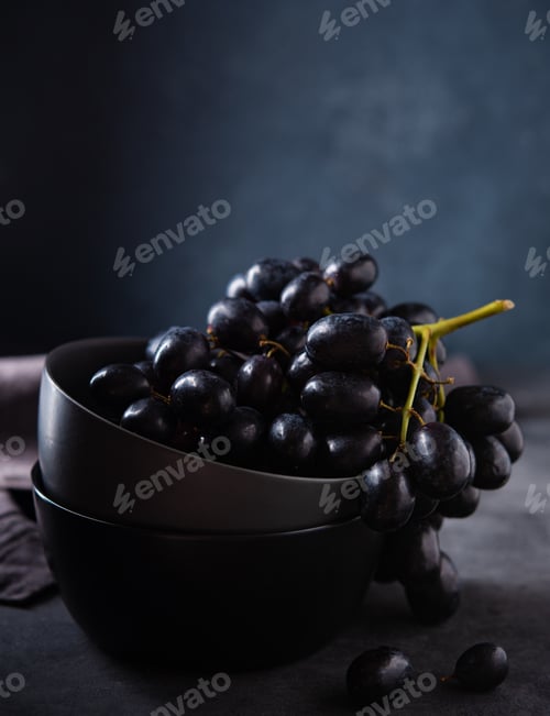Preview: a cluster of juicy black grapes lies in a dark gray bowl on a dark gray table