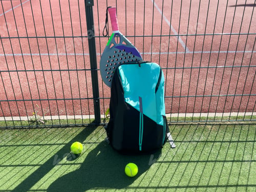 Preview: Blue bag with tennis padel racket and ball on grassy field at tennis court, copy space. Unaltered