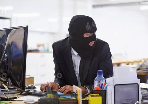 Preview: Doing some illegal activities...Shot of a hacker dressed in a black mask hacking a computer.