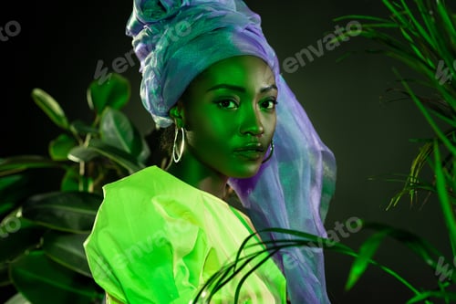 Preview: stylish african american woman in traditional wire head wrap under green light behind leaves