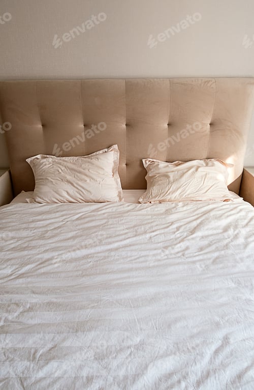 Preview: Beige tufted headboard with pillows and bedding in a cozy bedroom. Comfort and relaxation concept.