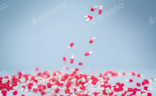 Preview: Selective focus on pink-white capsule pill fall down to white table. Antibiotic drug use