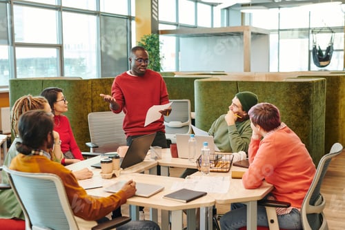 Preview: Medium group of young intercultural designers looking at African businessman