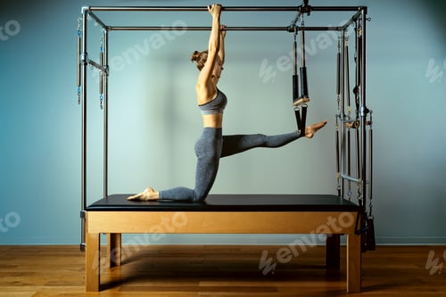 Preview: Young girl doing pilates exercises with a reformer bed. Beautiful slim fitness trainer on reformer