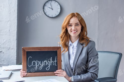 Preview: Smiling female lawyer looking at camera, while showing chalkboard with copyright lettering at