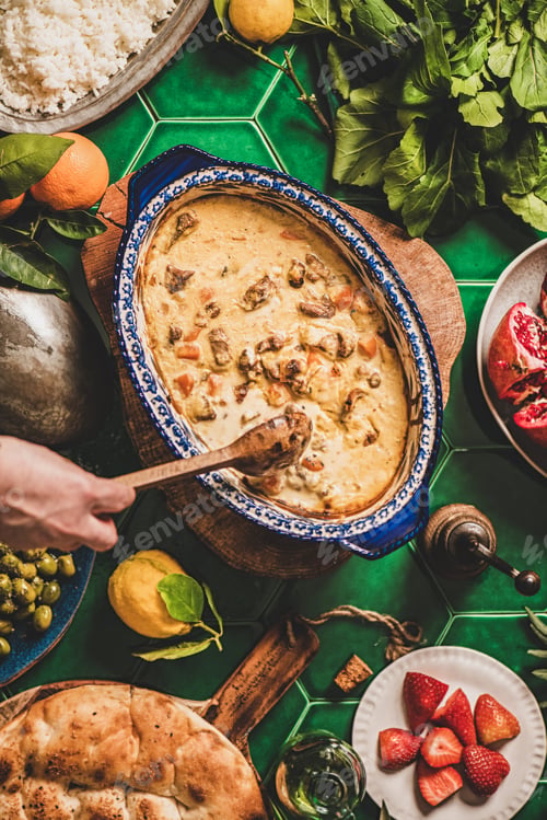 Preview: Female hands stirring Turkish lamb in sauce over green table