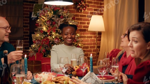 Preview: Woman at Christmas dinner table clinking glasses with family member while smiling at camera