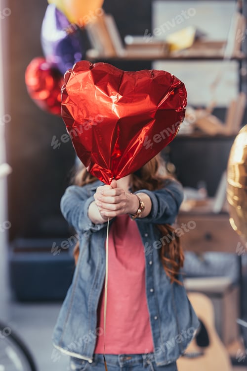 Preview: young woman holding red balloon and standing after party