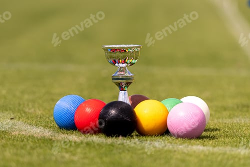 Preview: a set of colored croquet balls and a winners cup on the green lawn before the game, closeup