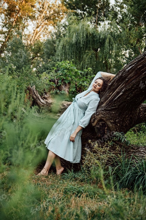 Preview: Nature and mental health. Barefoot woman in a dress is resting near the trees in nature