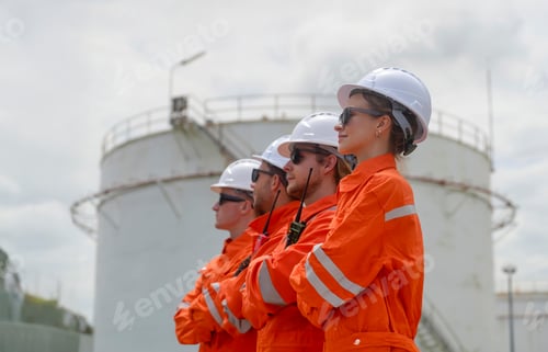 Preview: Team of workers in orange uniforms and helmets stands confidently at industrial location