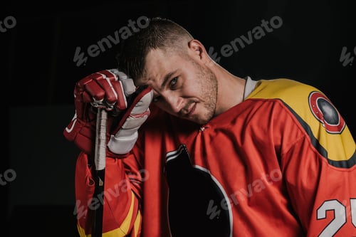 Preview: young hockey player leaning at hockey stick and looking at camera isolated on black