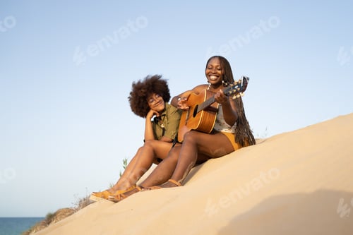 Preview: Cheerful girlfriends with guitar on beach