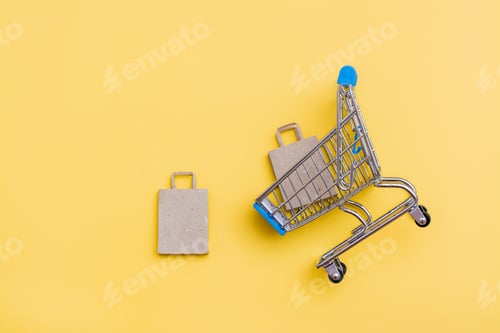 Preview: Eco-friendly craft paper bag in a metal shopping cart and near it on a yellow background.