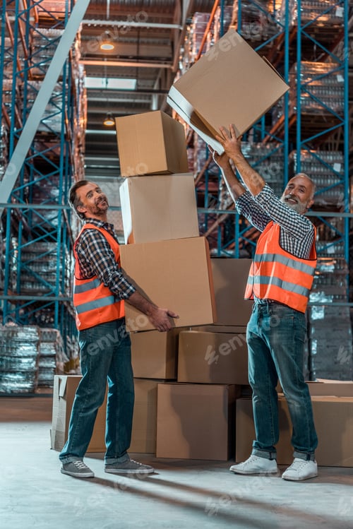Preview: smiling warehouse workers holding stacked boxes and looking at camera