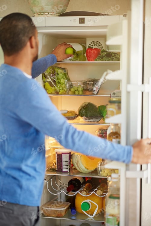 Preview: Rearview shot of a man opening a fridge filled with healthy food at home