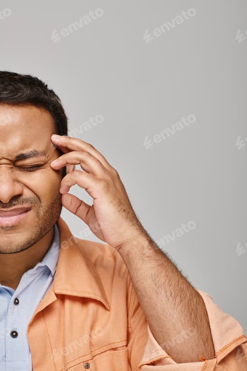 Preview: good looking indian man in orange vibrant jacket suffering from headache on gray background