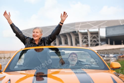 Preview: Senior couple enjoying cabriolet ride in city. Woman with wide open arms