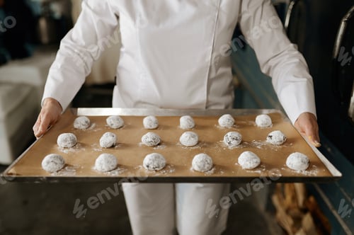 Preview: A baker carrying tray with cookies shaped from dough