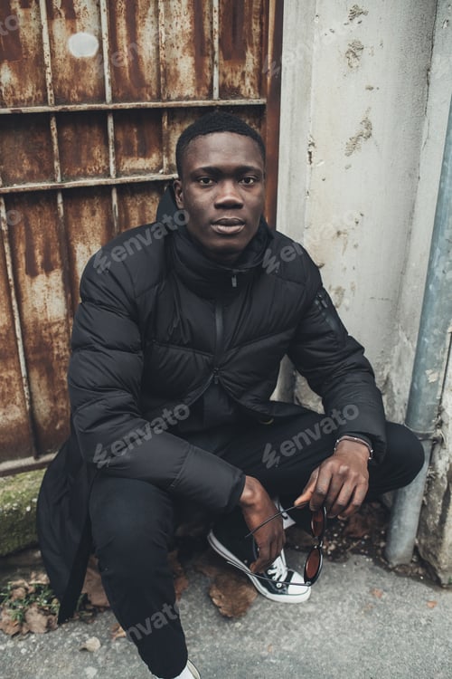 Preview: portrait of young black man sitting in the street and looking camera