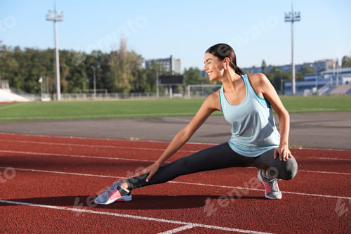 Preview: Young sportswoman with wireless earphones stretching at stadium