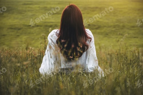Preview: Back view of a woman sitting alone in the park with with beautiful grass flower background