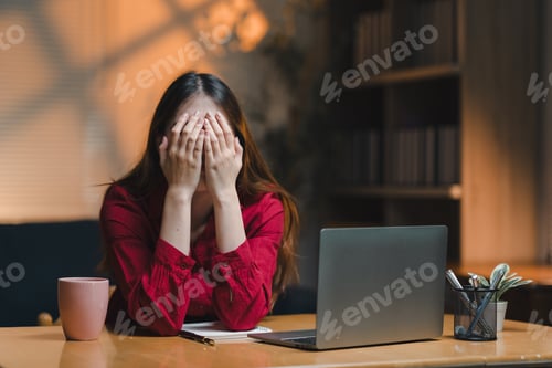 Preview: Stressed asian freelancer covering face with hands at home office desk
