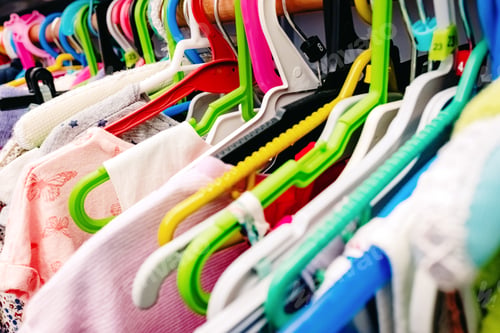 Preview: Colorful children's dresses hanging on hangers in a closet.