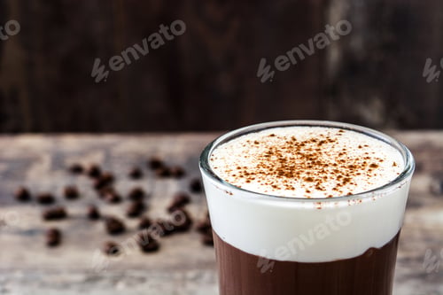 Preview: Creamy coffee drink topped with cinnamon and coffee beans scattered on wooden table