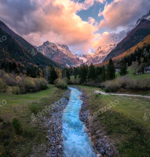 Preview: Stream in mountain valley with autumn trees, snowy peak at sunset
