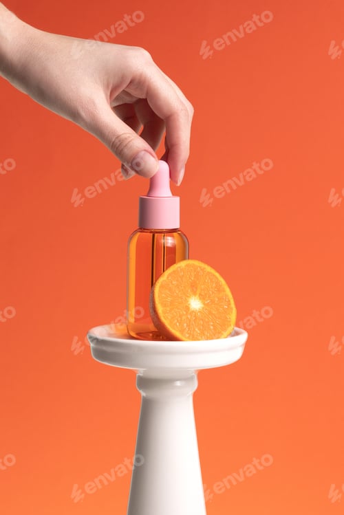 Preview: Woman hands holding facial essential oil or serum packaging on orange background.