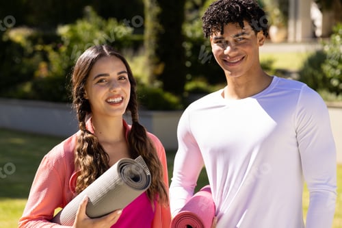 Preview: Portrait of happy fit diverse couple standing in sunny garden holding yoga mats
