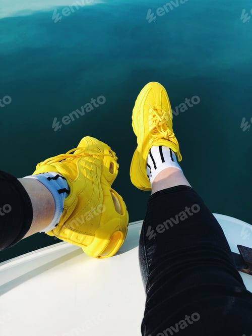 Preview: legs in yellow sneakers and trendy socks on the the boat against the background of turquoise water