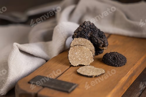 Preview: Whole and sliced black truffles mushroom on wooden board on dark brown table, close up