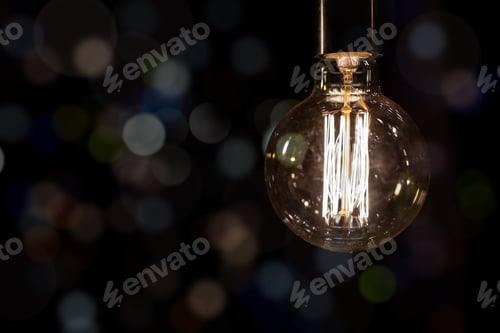 Preview: Glowing vintage old one tungsten lightbulb hanged on ceiling against black wall bokeh background
