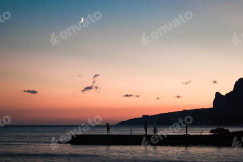 Preview: Beautiful sunset with moon in sky and man fishing on dock