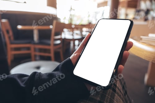 Preview: Mockup image of hands holding black mobile phone with blank white screen in cafe