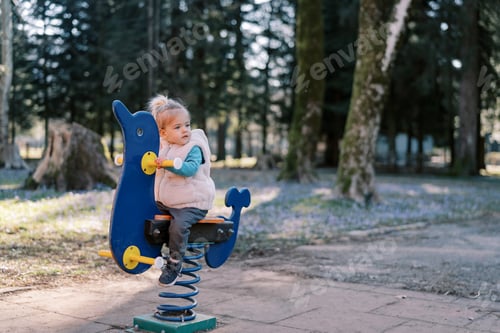 Preview: Little girl sits on a spring swing and looks away