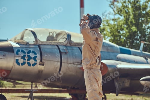 Preview: Mechanic in uniform and flying helmet standing near an old war fighter-interceptor