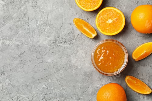 Preview: Oranges and glass jar with jam on gray background, top view