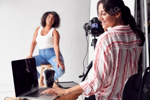 Preview: Female Photographer In Digital Studio Shooting Images On Camera Tethered To Laptop Computer